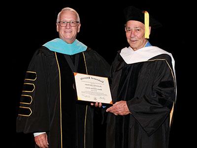 杰瑞·谢德格穿着黑色博士袍，戴着白色兜帽, 身穿黑色博士袍，头戴蓝色兜帽的波特校长授予他荣誉博士学位.